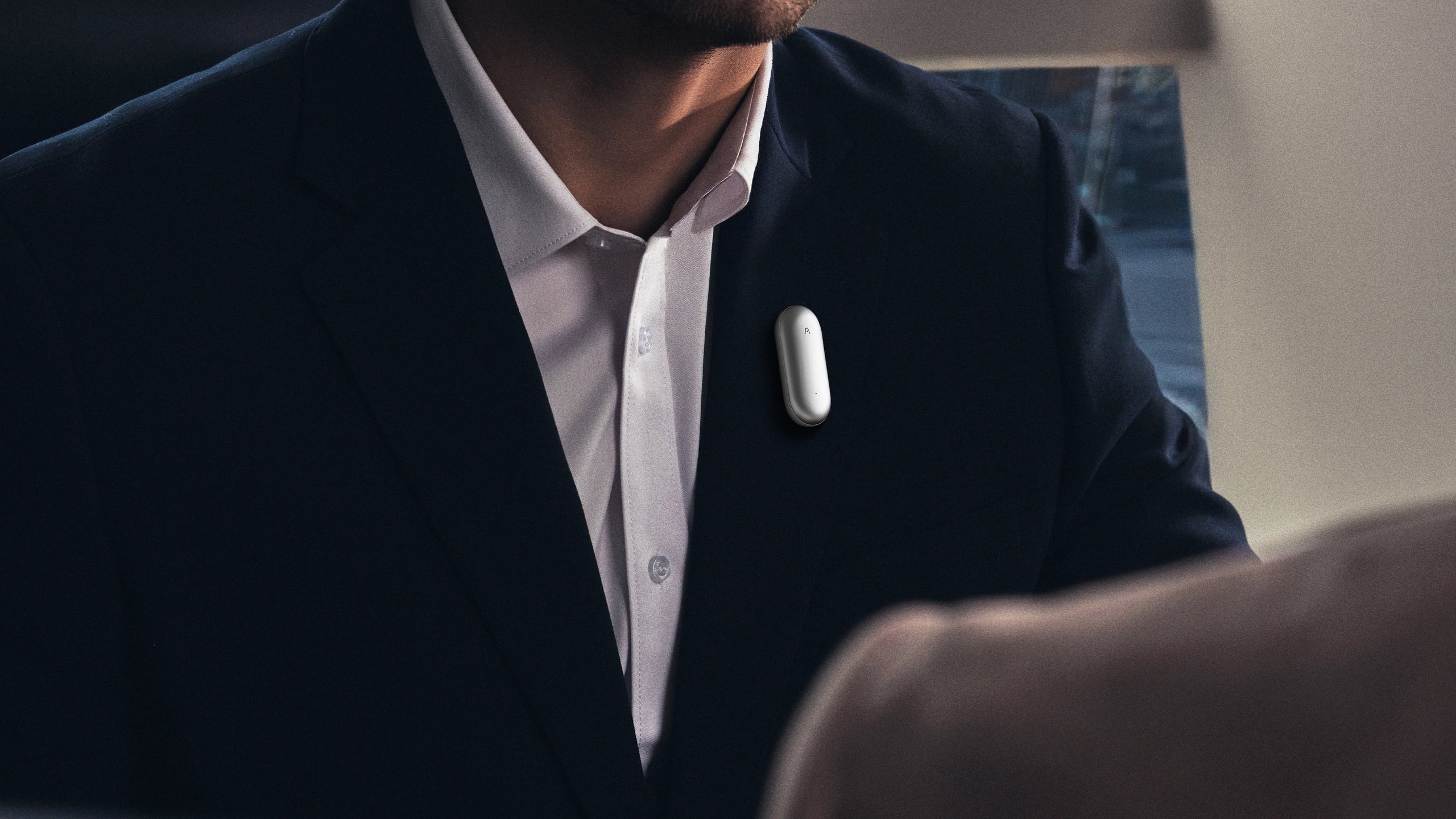 Silver Plaud NotePin AI voice recorder worn on a man's suit lapel.