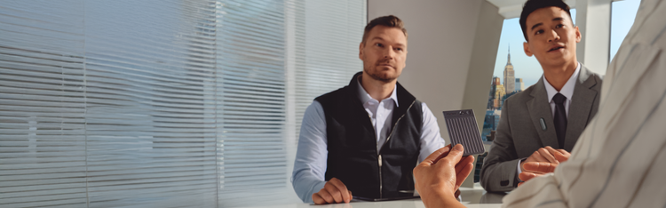 A person holds a black Plaud Note Pro during a business meeting with two colleagues in a modern office.