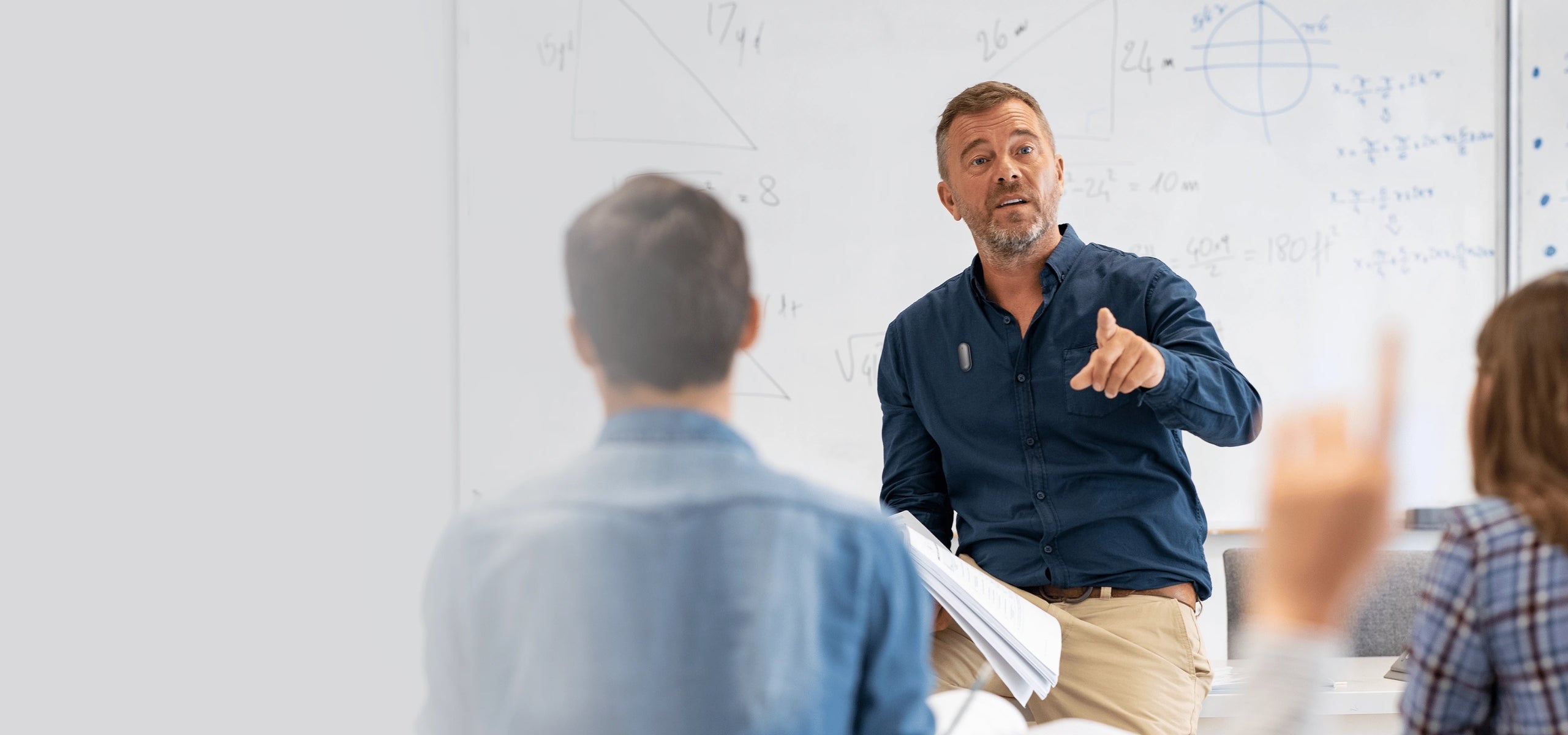 A lecturer wearing a silver Plaud NotePin on his shirt while teaching a class in front of a whiteboard.