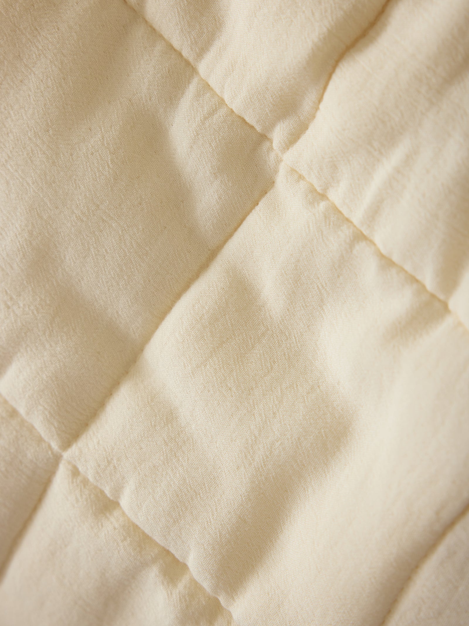 Close up of Buttermilk Aire Bamboo Box Quilt Euro Sham. The sham is resting on a bed in a bedroom