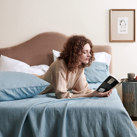 Woman reading a book on her bed, which is wrapped in a blue Bedsure Linen Sheet Set