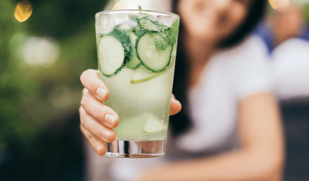 a woman holding a glass of chilled cucumber water