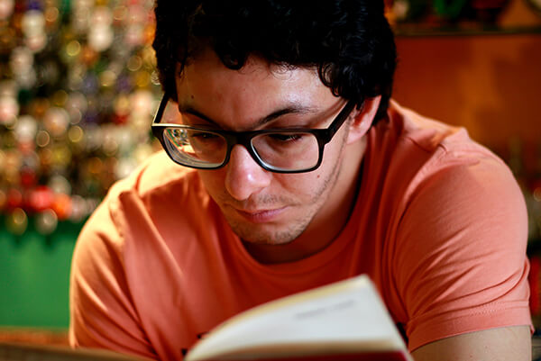 A man with glasses is reading, but it looks a little difficult.