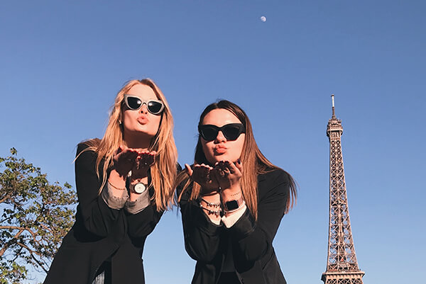 Two girls wearing sunglasses blow happy kisses