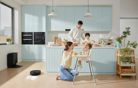 Parents feeding child, Roborock vacuum cleaning food debris.