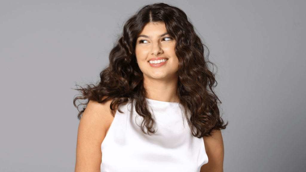 Smiling woman with naturally curly hair styled to perfection, showcasing at-home haircare routine success.