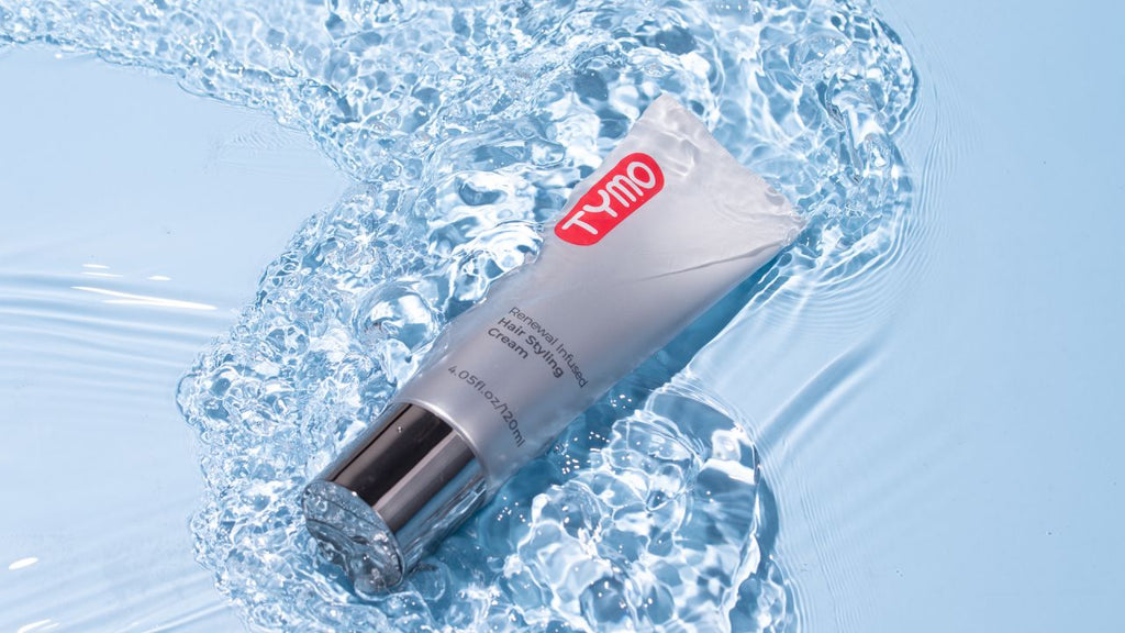 Tube of TYMO hair styling cream against a vibrant blue water background, symbolizing hydration and care.