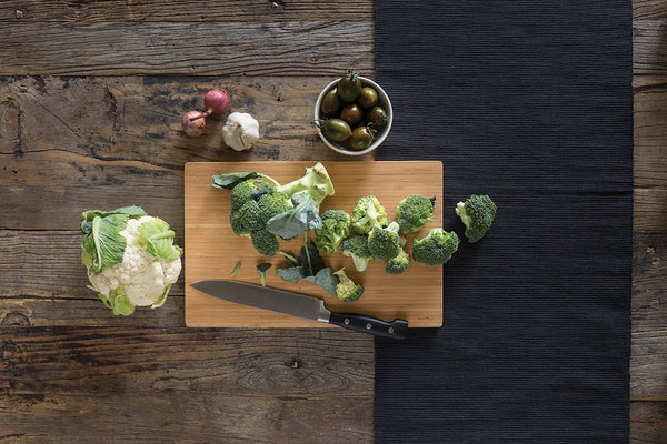 竹菜板是木质桌面。有一头花椰菜,一些切碎的花椰菜,和其他蔬菜,在砧板。一把刀也取决于砧板。