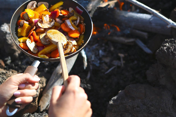 一个人在锅在篝火上做饭。竹勺混合搅拌蔬菜为他们做饭。