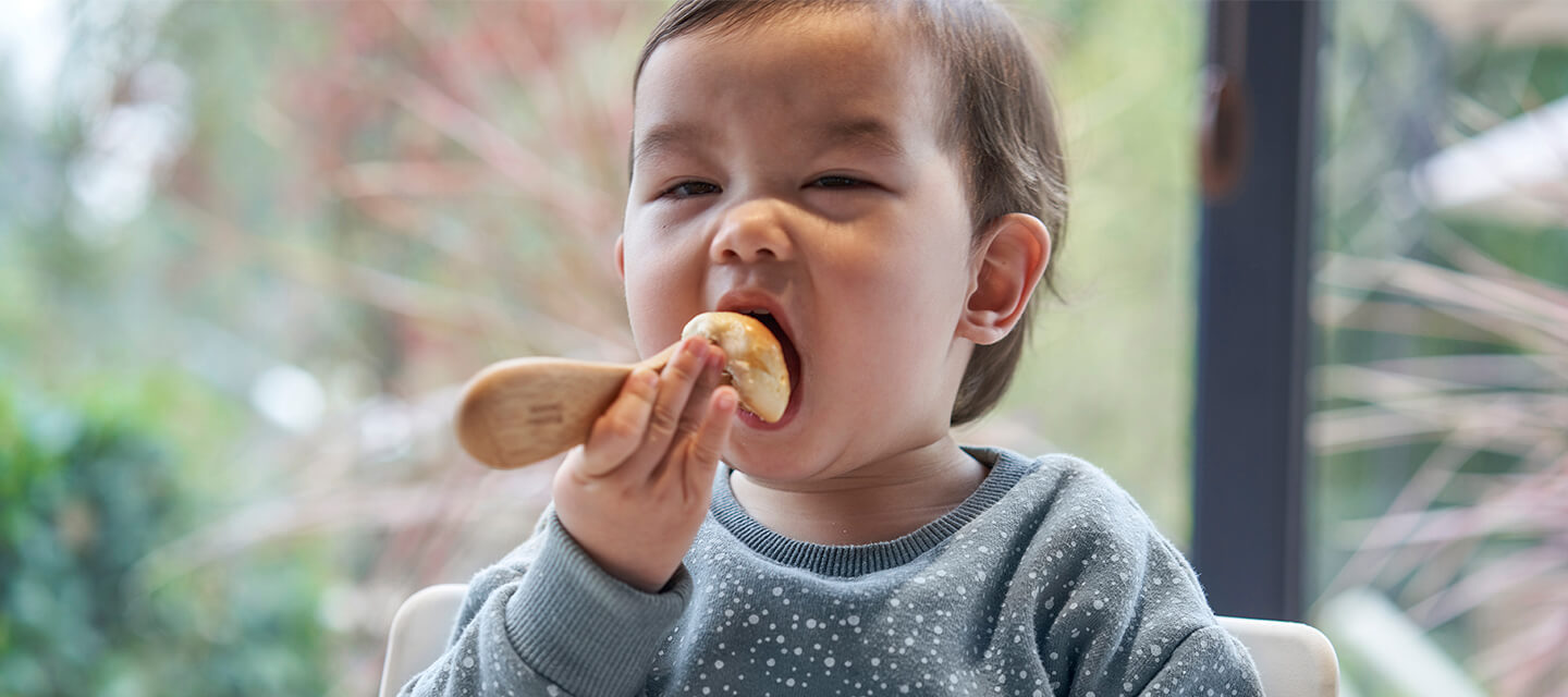 一个小孩在一个蓝色的毛衣用竹婴儿用具一起吃饭。