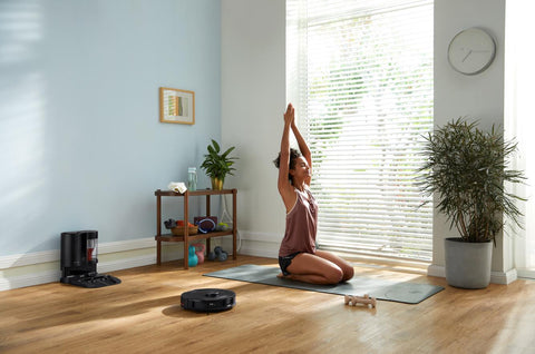 Une fille fait du yoga sur le sol de sa maison pendant que l'aspirateur Roborock à côté d'elle nettoie le sol et évite intelligemment sa place.