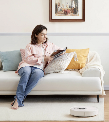 L'aspirateur de Roborock nettoie tranquillement la poussière du tapis et la dame lit un livre à côté de lui.