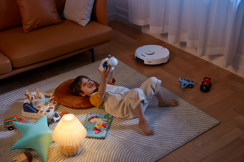 Kleiner Junge liegt auf dem Boden und spielt, während der Staubsauger von Roborock automatisch den Boden neben ihm reinigt