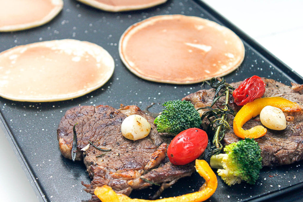 Black griddle with steak and pancake on it