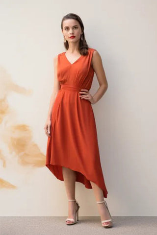 A white woman wears a burnt orange dress and beige mid-heeled shoes