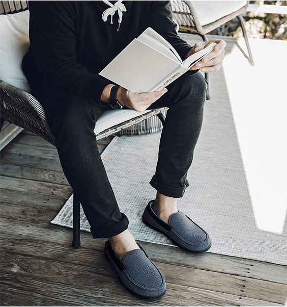 The model wears slippers and reads a book while sitting on a chair in the yard