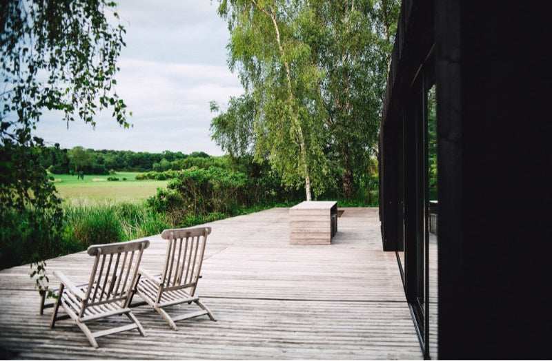 two wooden deck chairs on a wooden deck outside looking over a field