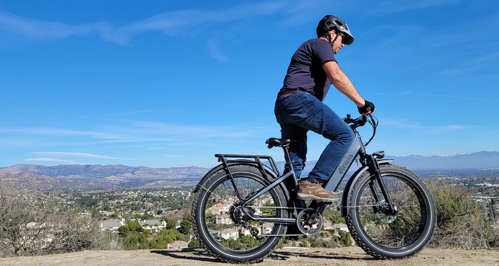 Man riding an electric bike with a backpack on a scenic hilltop under a clear blue sky.