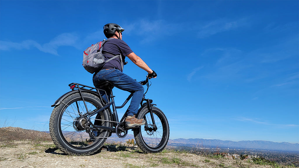 Man riding an electric bicycle on a scenic overlook with mountains in the background.