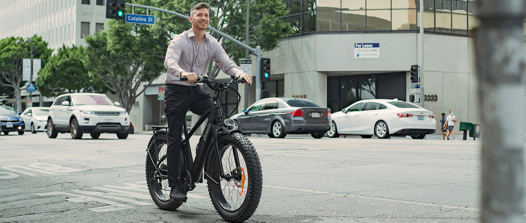 Man riding an electric bicycle on a city street with cars and buildings in the background.