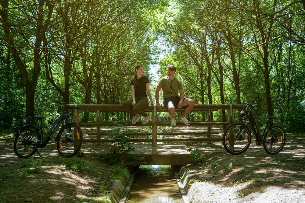 a young couple sit on the fence over the river, leaving their ebikes besides