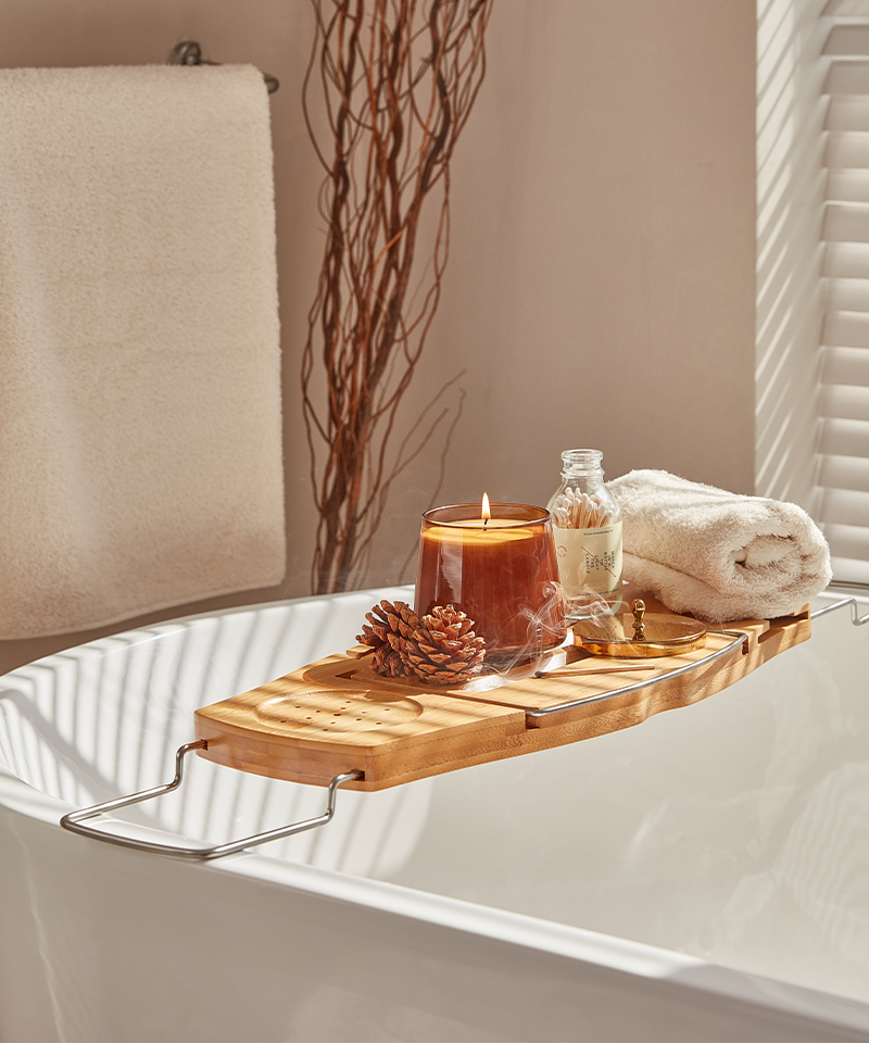 Brown candle on bath tray with towel, matches, and pinecone