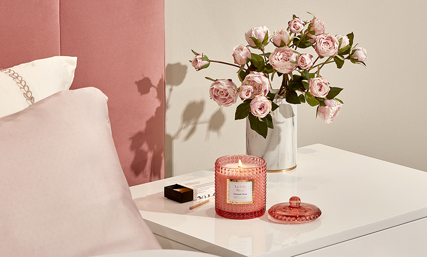 Damask rose candle on bedside table with a vase of roses