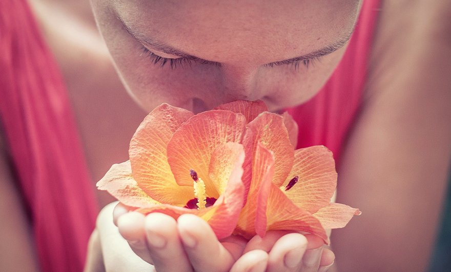 woman in pink tank top smelling pink and yellow flower