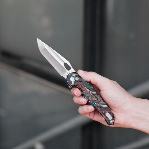 A hand holding a Vosteed Thunderbird pocket knife with a colorful swirl pattern handle and a tanto blade