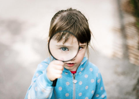 A girl in blue semantic holding a magnifying glass