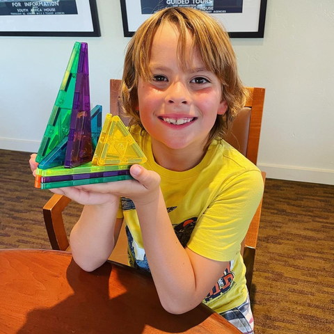 a boy is holding a magnetic tiles tower