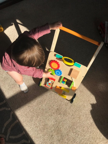 a toddler is using cossy wooden walker car