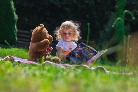A toddler is reading books with a teddy bear