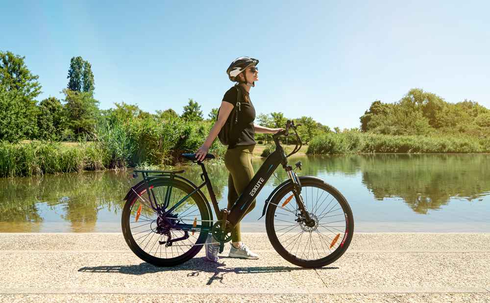 een dame met helm die met haar elektrische trekkingfiets bij het meer staat