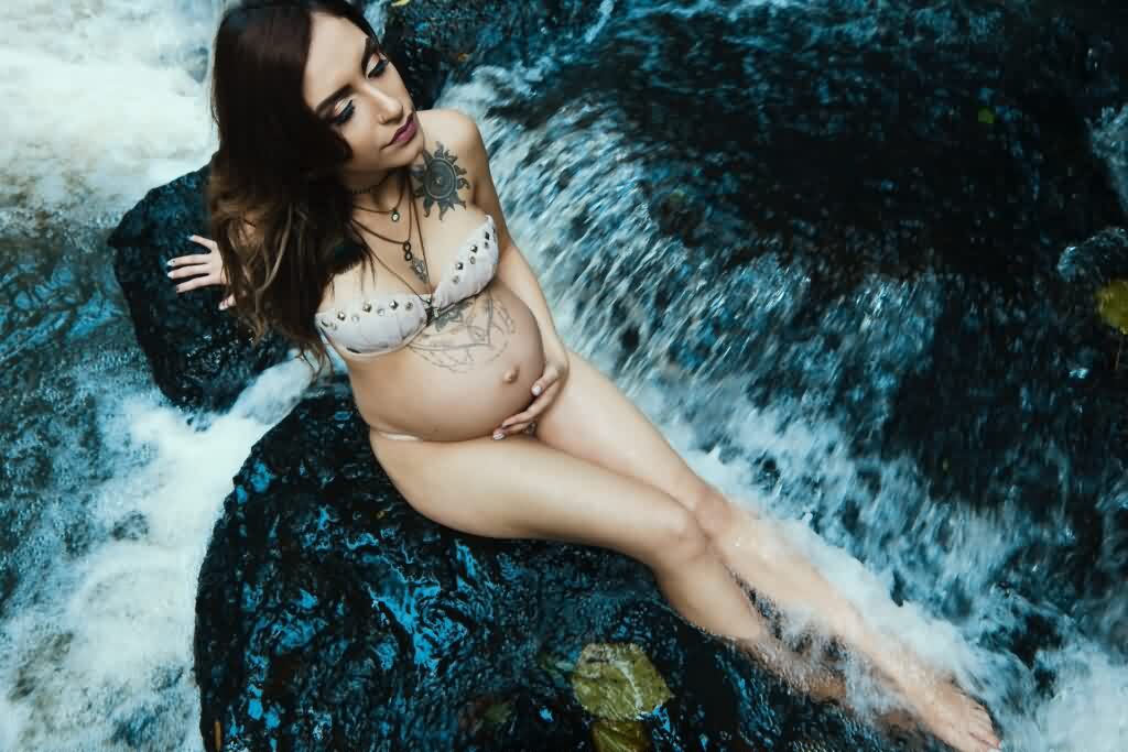 pregnant woman sits on rock in running spring