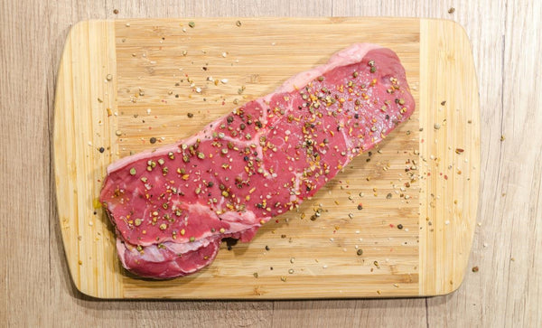 a piece of beef on a wooden chopping board covered in seasoning