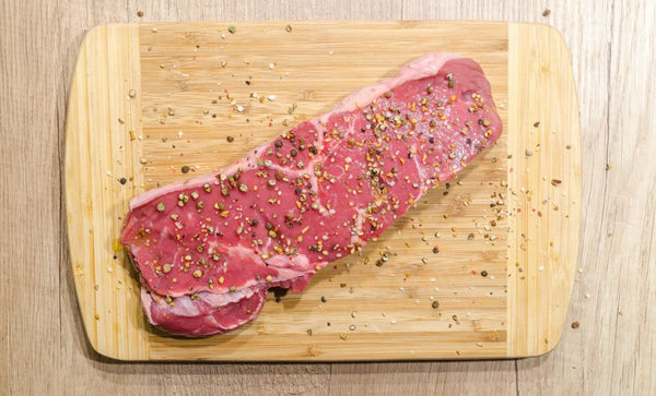 a piece of beef on a wooden chopping board covered in seasoning