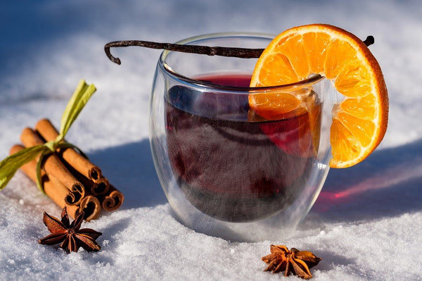 glass of mulled wine with a cut orange piece on the cups rim next to cinnamon sticks
