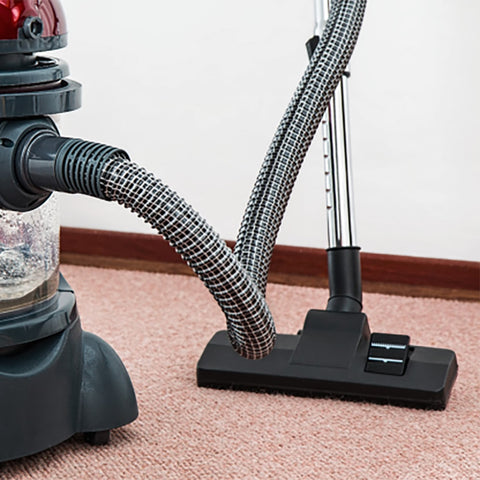 Pink carpet squares cover the room, and a black vacuum cleaner is working on the carpet!