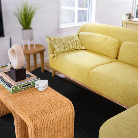 There is a yellow sofa on the black carpets with padding in a cozy room.