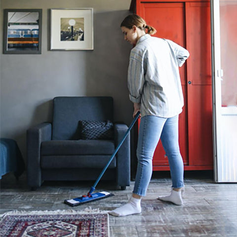 There's a lady who's cleaning up, and next to her is an area rug and a gray solo sofa.