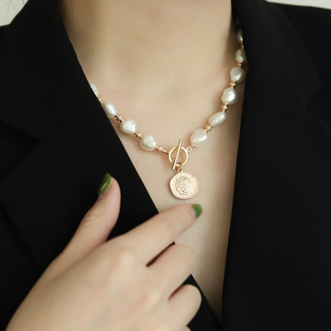 Women in black suit wear barouque pearl necklace.