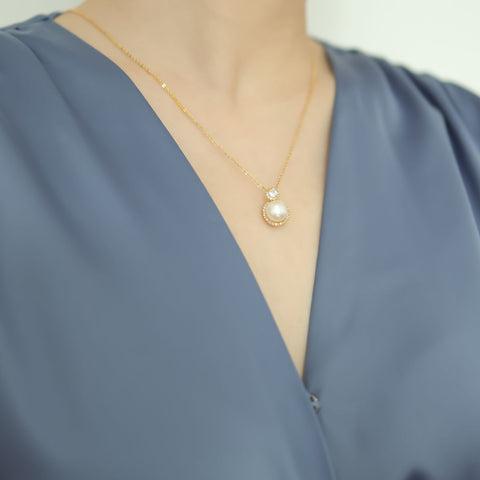 Women in blue dress wear diamond pearl pendant.