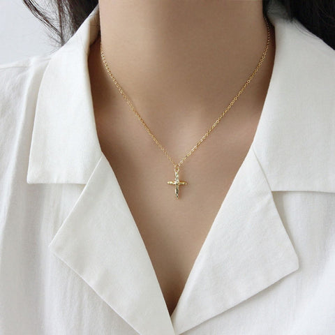 Women in white suit wear gold cross pendant.
