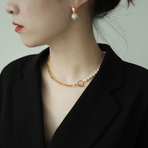 Women in black wear half pearl half chain toggle necklace.