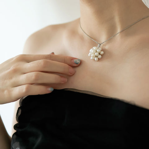 Women in black dress wear white freshwater pearl necklace.