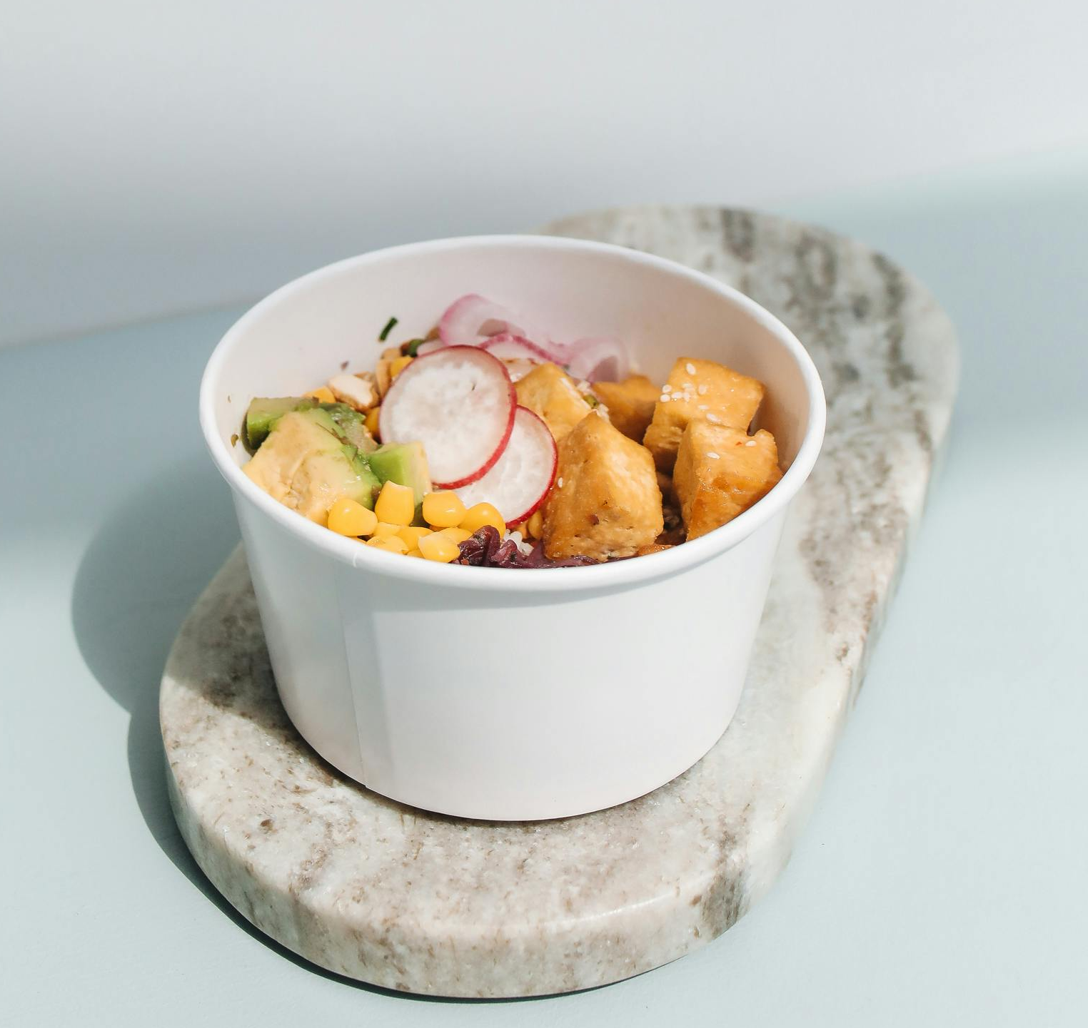 Colorful meal in white paper bowl with food on marble surface.