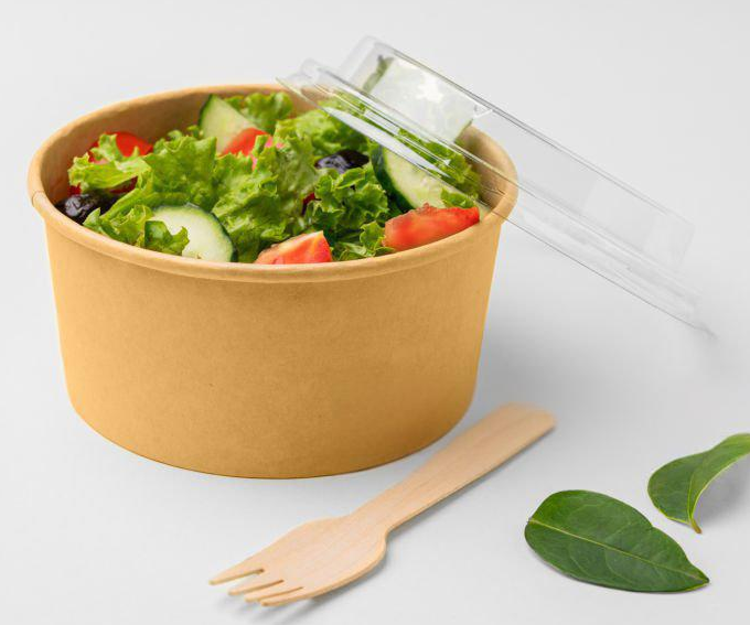 Fresh salad with lettuce, cucumber, tomato, and olives in brown paper bowl with clear lid, wooden fork beside; healthy meal vibe.