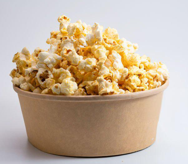 Golden popcorn piled high in a light brown paper bowl on white background.