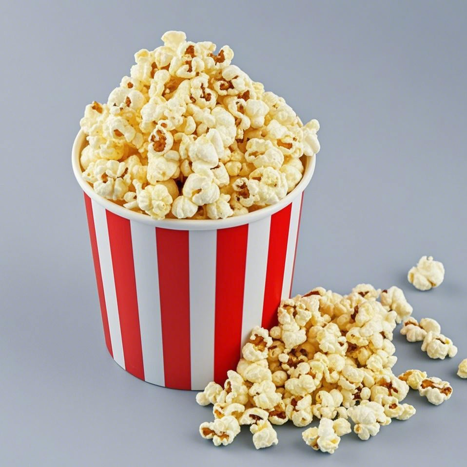 Paper bucket of popcorn with some spilled kernels on a gray background